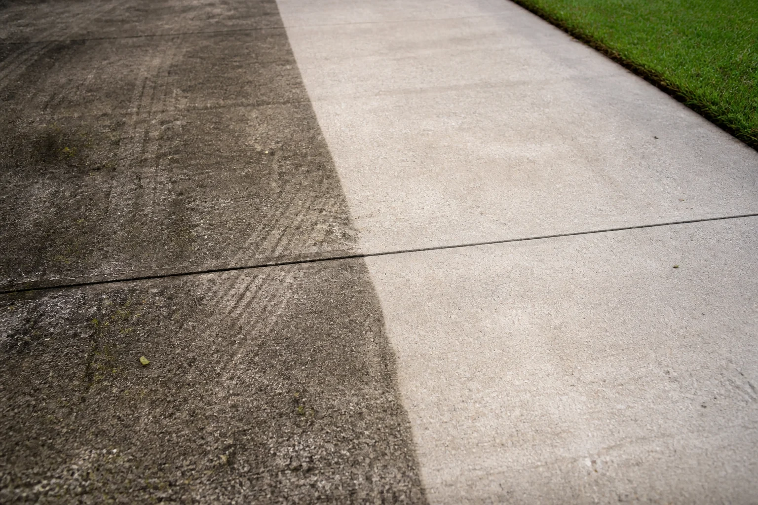 A concrete driveway half cleaned, one bright stripe cut through years of grime.